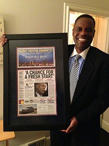 A man in a suit stands holding a newspaper