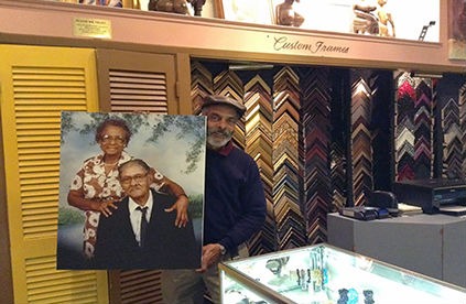 A man stands in a store, holding a framed photo of his parents