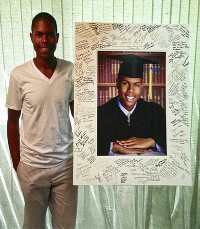 A young man smiles proudly while holding his framed diploma