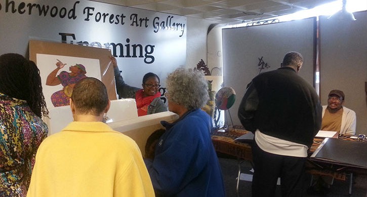 Visitors engage with staff at the Sherwood Forest Art Gallery, discussing art pieces and framing options in a vibrant community setting.