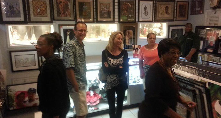 Visitors explore an art gallery filled with framed artwork and display cases, engaged in conversation and observing the exhibits.