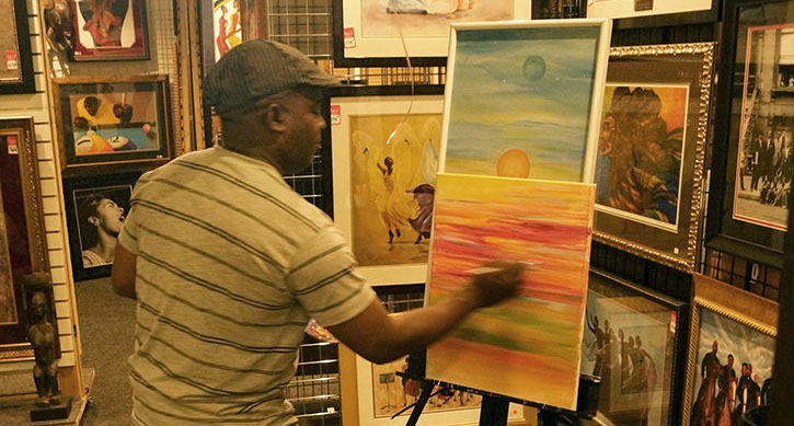 An artist creates a colorful abstract painting at an art gallery, surrounded by various framed artworks. The scene highlights creativity and artistic expression.