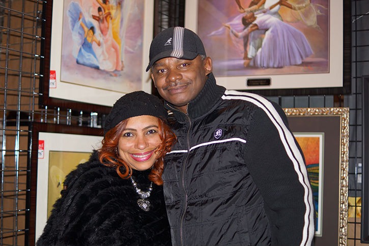 A smiling couple poses together in front of vibrant art pieces, showcasing their connection amid a gallery setting.
