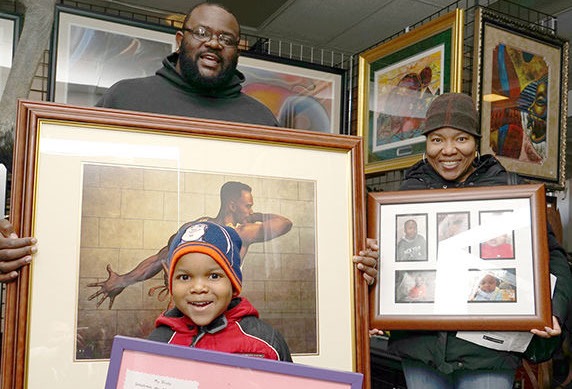 A man and woman hold framed artwork, while a young boy smiles with a colorful certificate. The setting showcases an artistic community event.